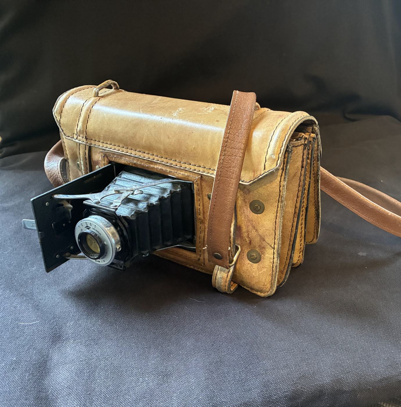 Pinhole camera: a worn tan leather case with a folding bellows camera opening from its side