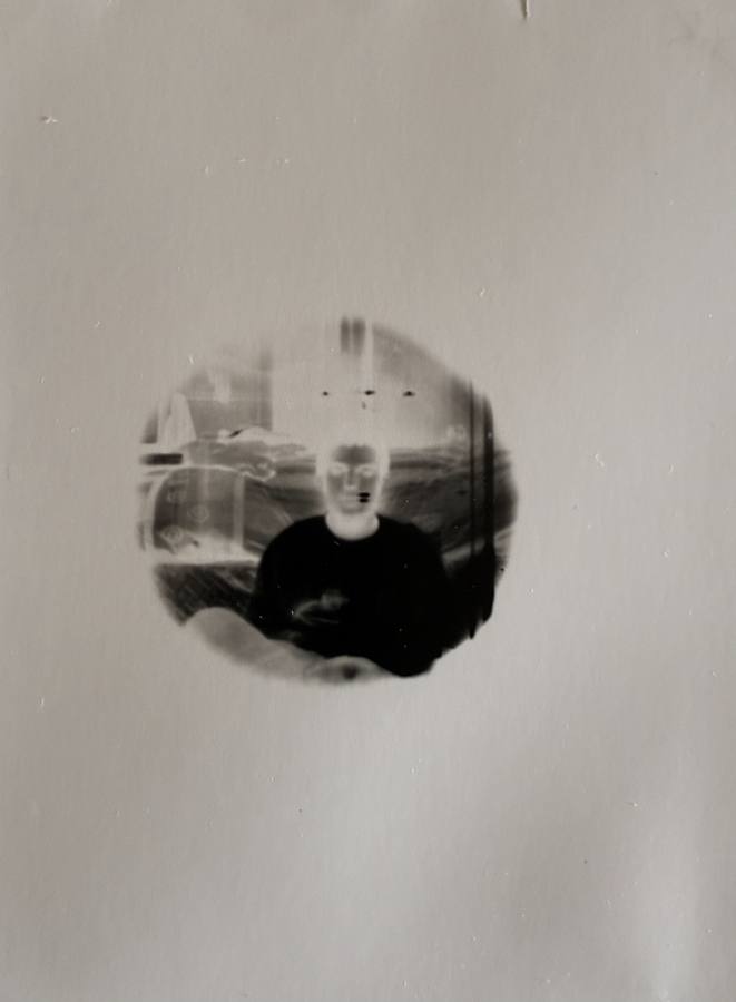 Pinhole photograph: a figure seated in a room, seen through a small round opening