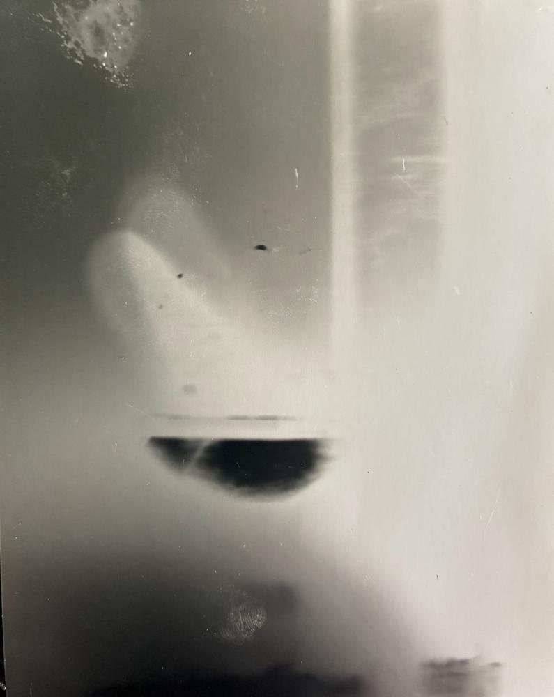 Pinhole photograph: a pale, blurred vertical frame with a dark half-moon shape hanging in the middle