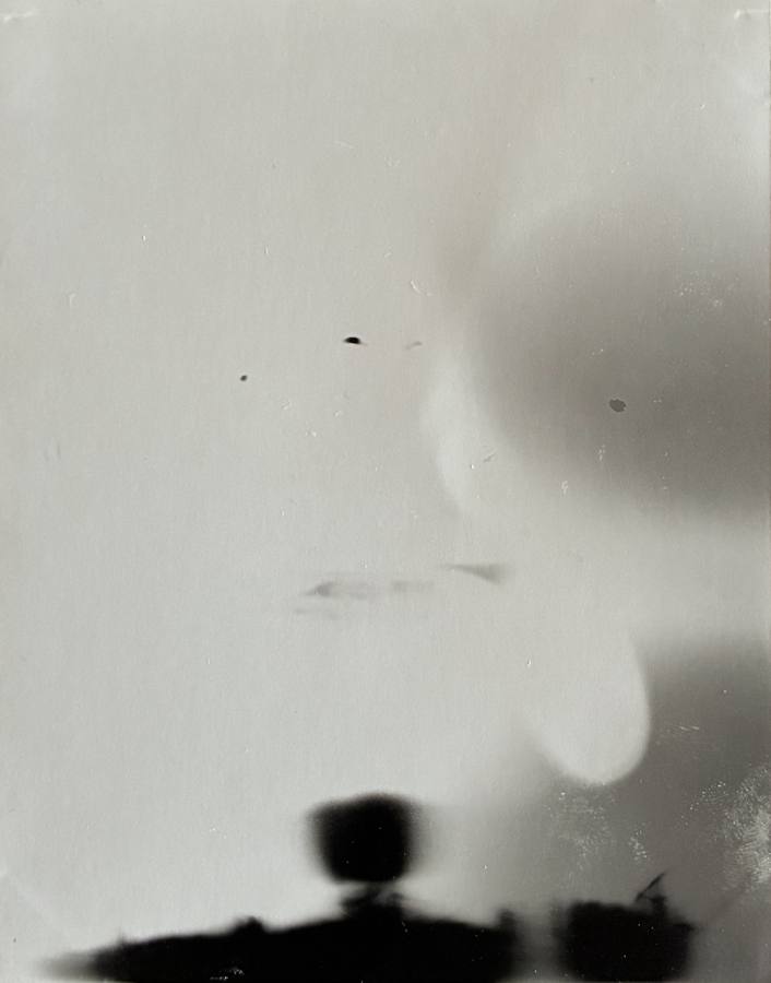 Pinhole photograph: pale soft shapes above a dark band of objects along the bottom edge